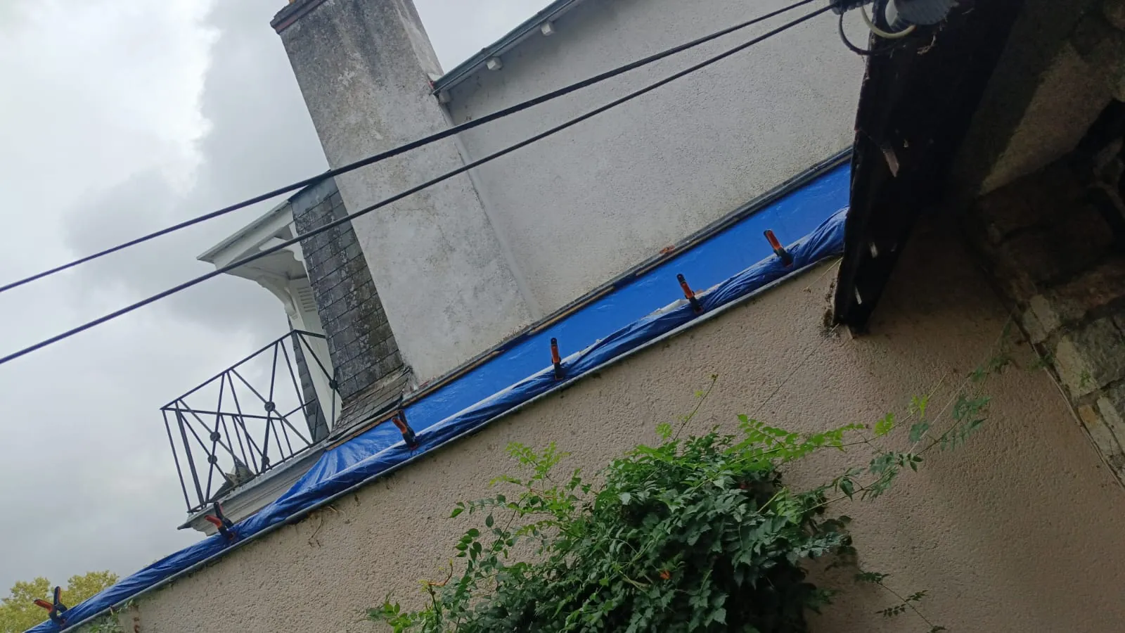 Bâche bleue tendue et lestée le long d'une génoise, en attente de la reprise définitive