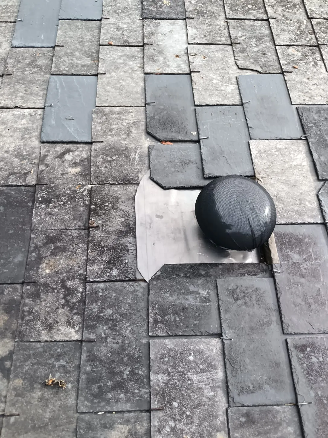 Chatière de ventilation neuve posée sur platine zinc, intégrée dans une couverture en ardoise