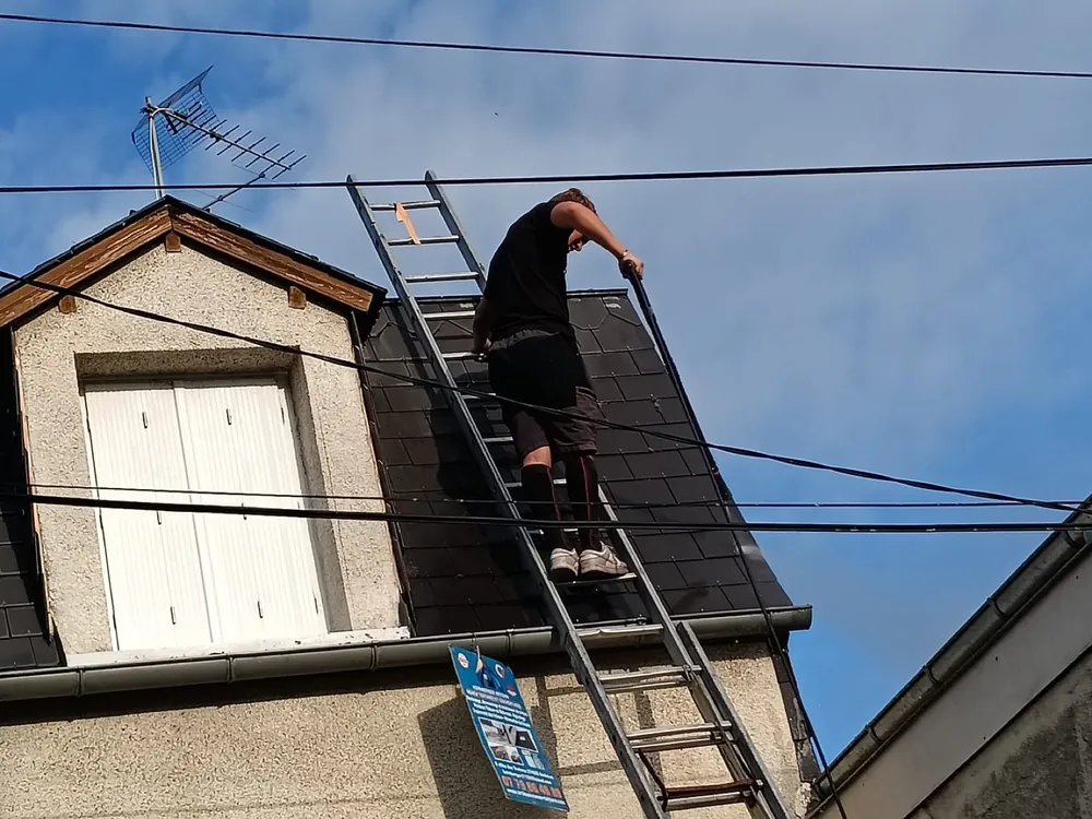 Couvreur en haut d'une échelle de toit sur une couverture ardoise avec lucarne, secteur de Tours