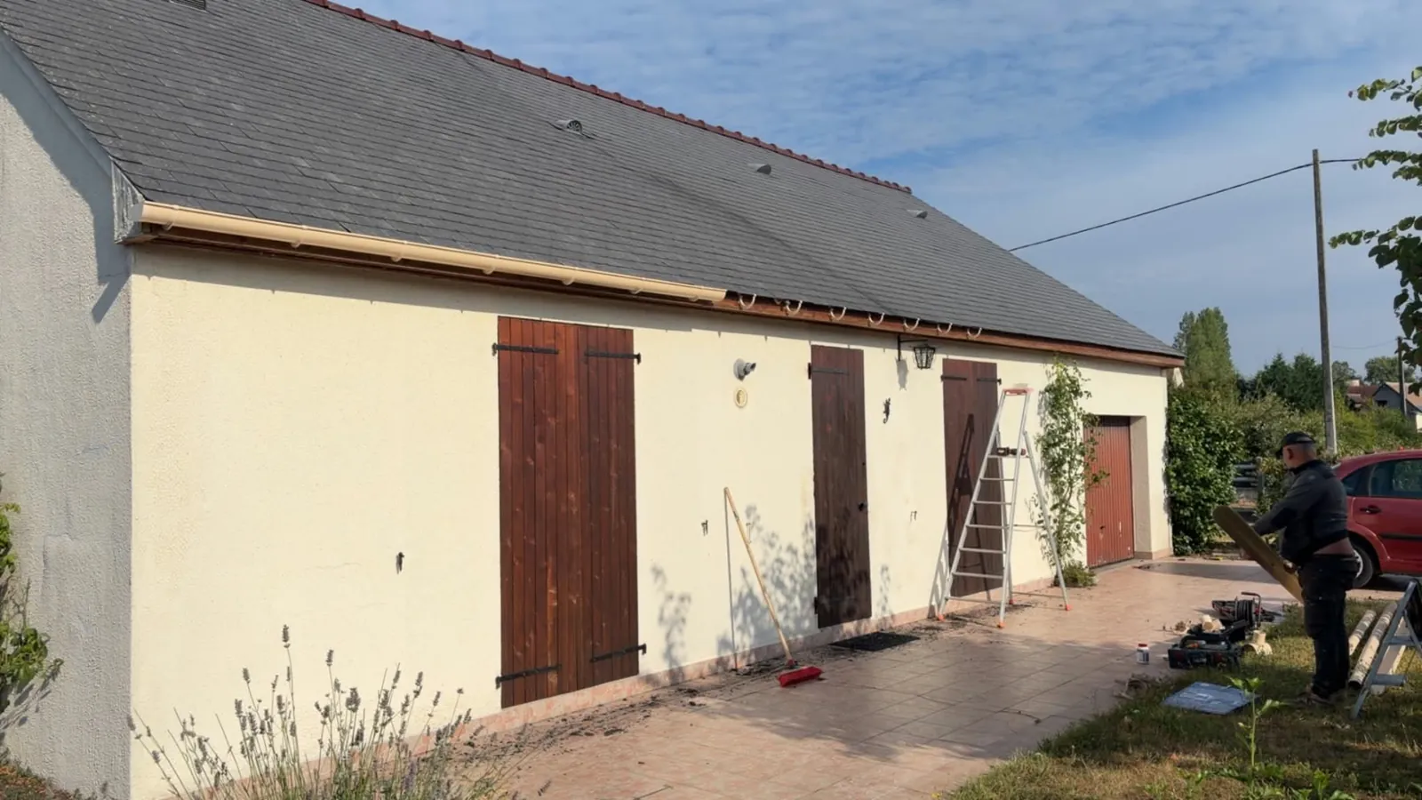 Maison de plain-pied avec toiture en ardoise nettoyée, couvreur qui ramasse les mousses tombées le long de la façade