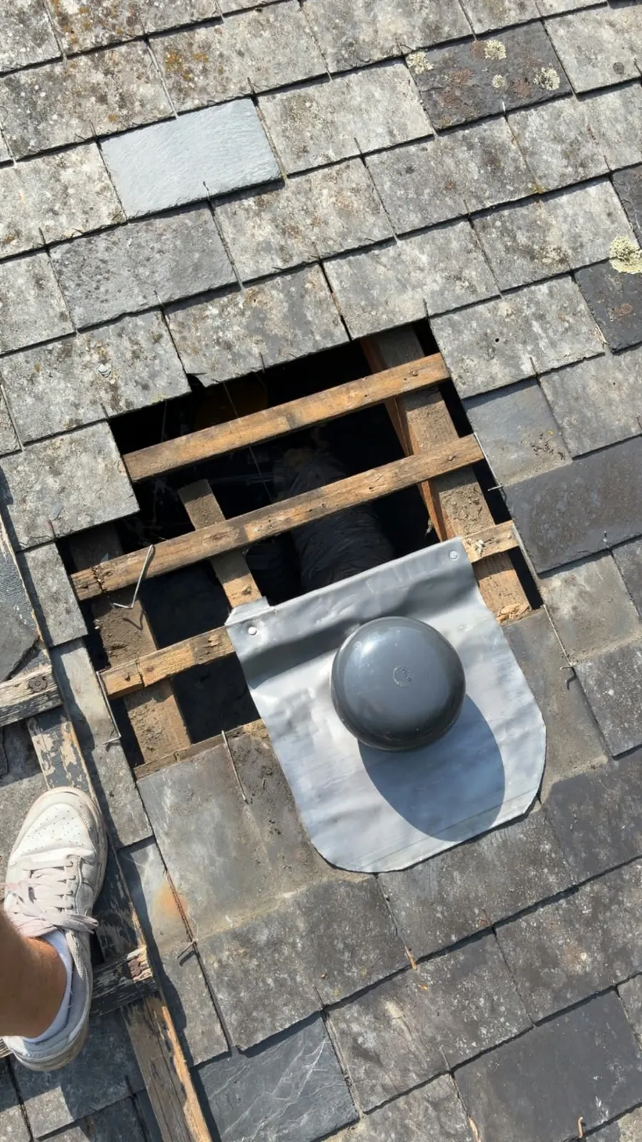 Nouvelle sortie de toit VMC posée sur ardoise : platine d'étanchéité grise fixée sur le liteau et chapeau de VMC anthracite, avant repose des ardoises du haut