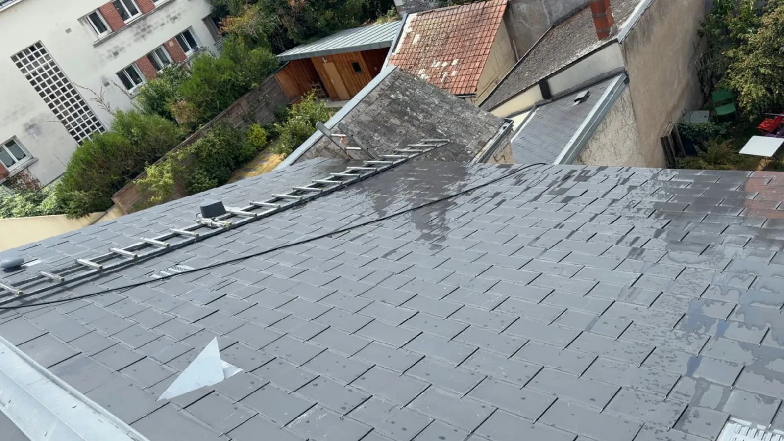 Toiture en ardoise nettoyée et rincée à Tours, échelle de toit posée sur le versant, à côté d'un petit toit voisin encore gris et couvert de lichens