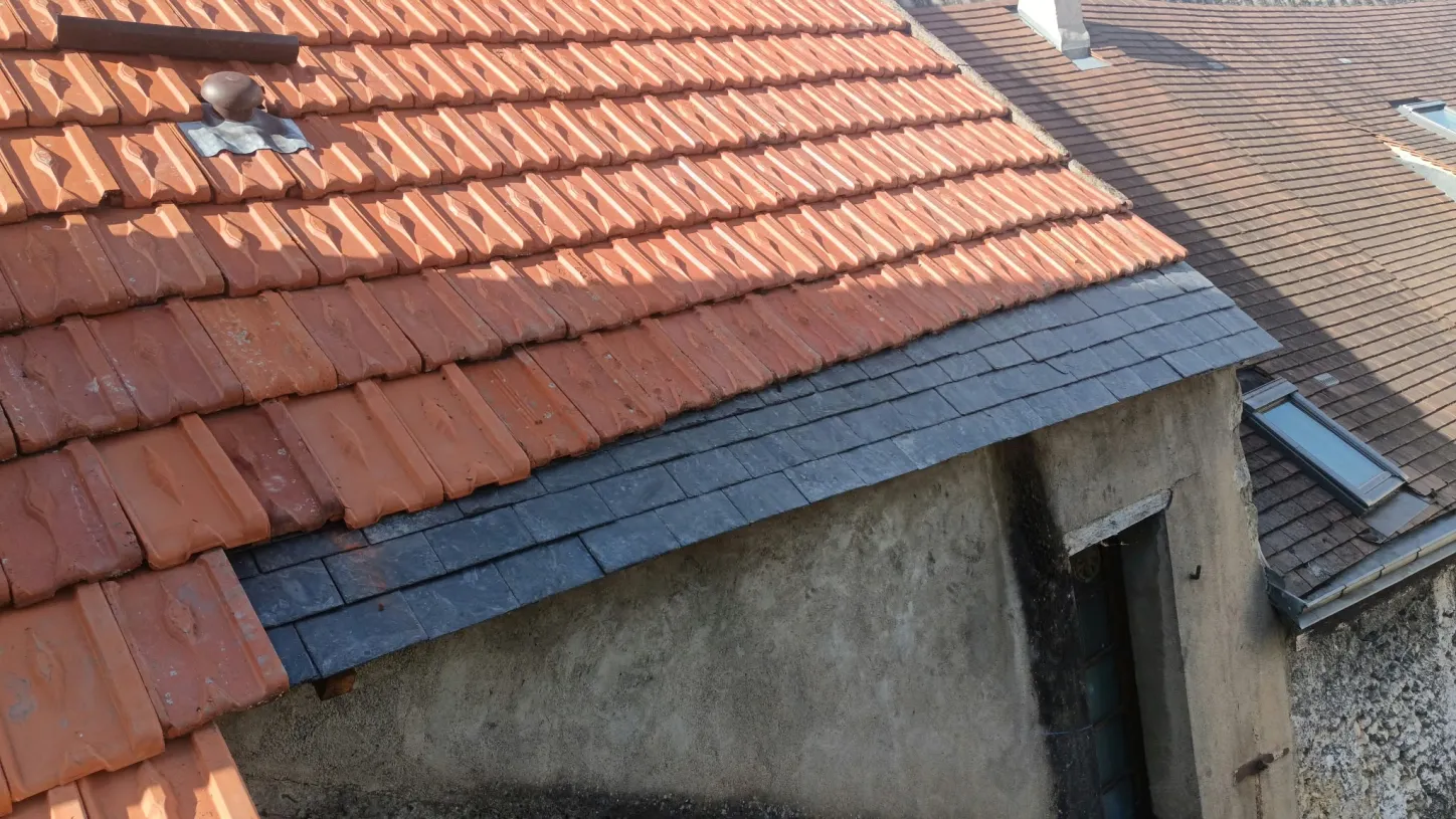 Bas de versant refait en ardoise sous les tuiles mécaniques, au-dessus d'un mur enduit, sur un chantier récent en Touraine