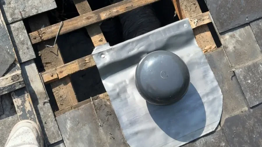 Sortie de toit VMC neuve sur une toiture en ardoise à Tours : chapeau gris anthracite sur sa platine d'étanchéité, ardoises déposées autour et liteaux visibles